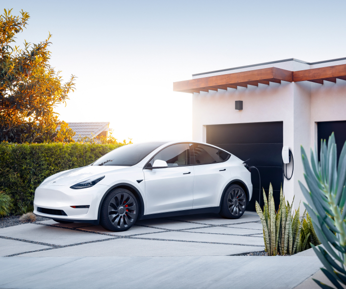 Tesla Model Y in ricarica con Tesla Wall Connector davanti a una villa moderna